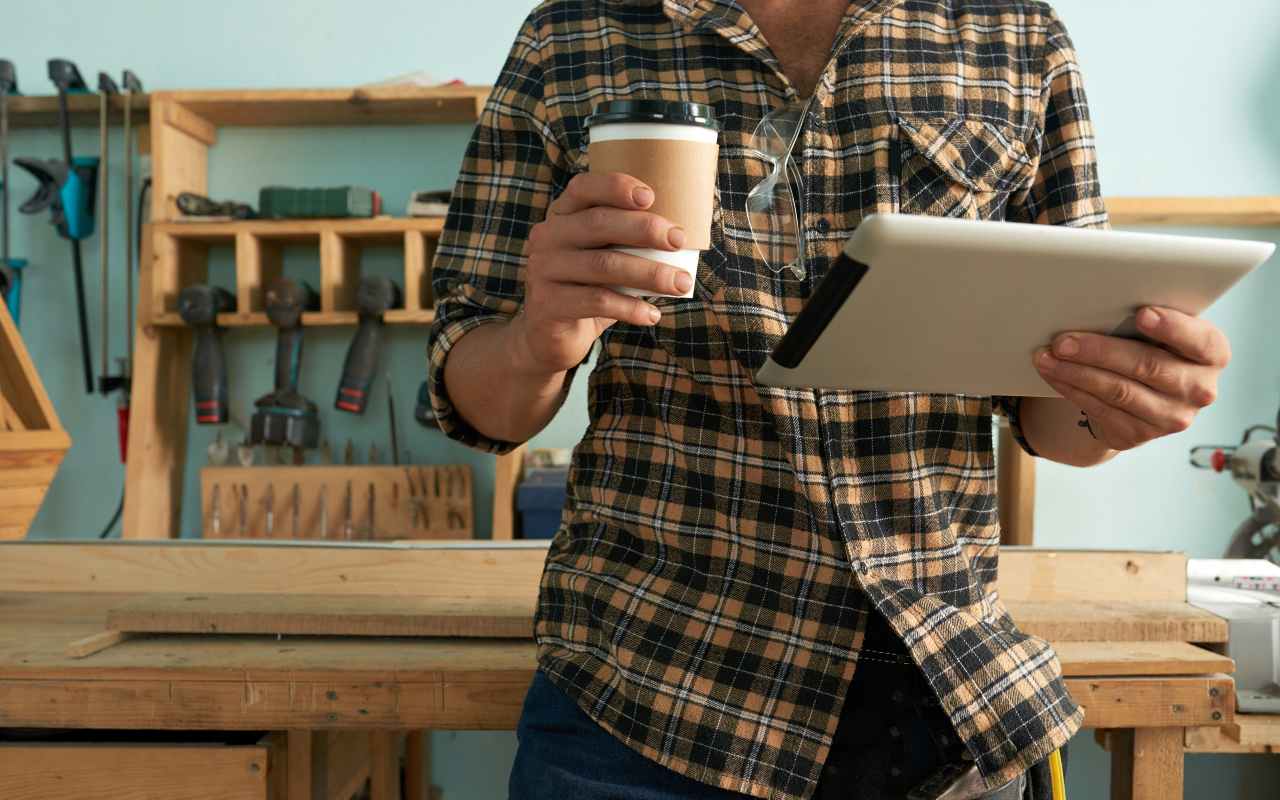 Una persona tiene in mano un caffè e un tablet nel suo laboratorio di fai da te