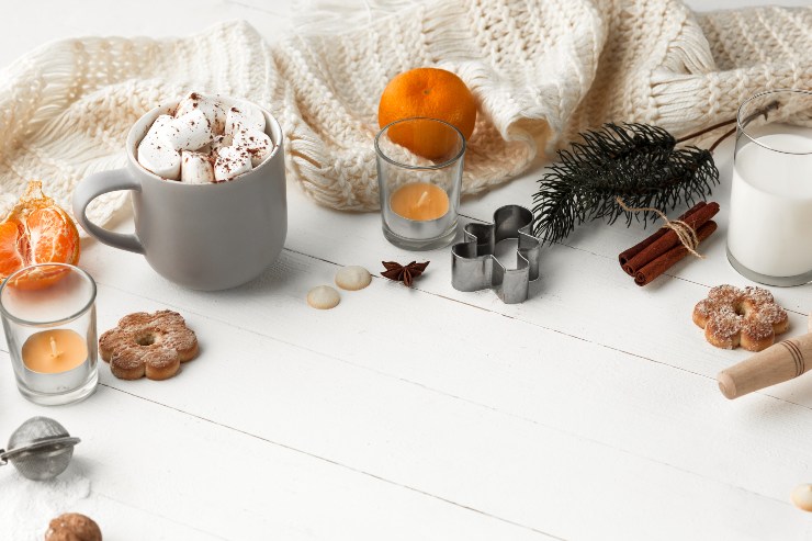 Biscotti, una tazza di cioccolata calda, mandarini, formine, un bicchiere di latte e candele su un tavolo