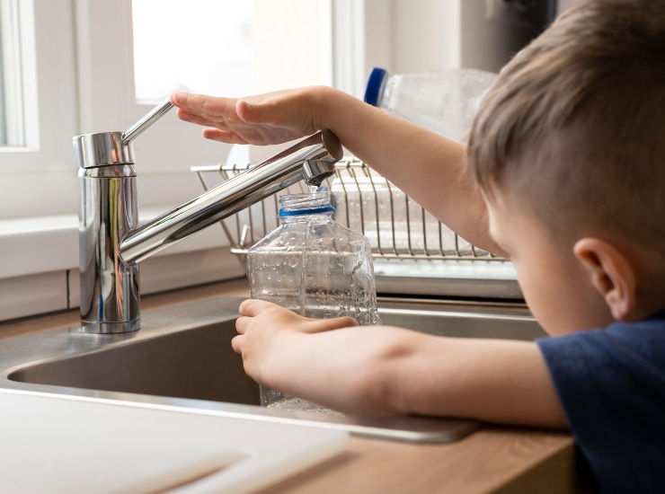 Un bambino riempie una bottiglia di plastica con l'acqua del rubinetto