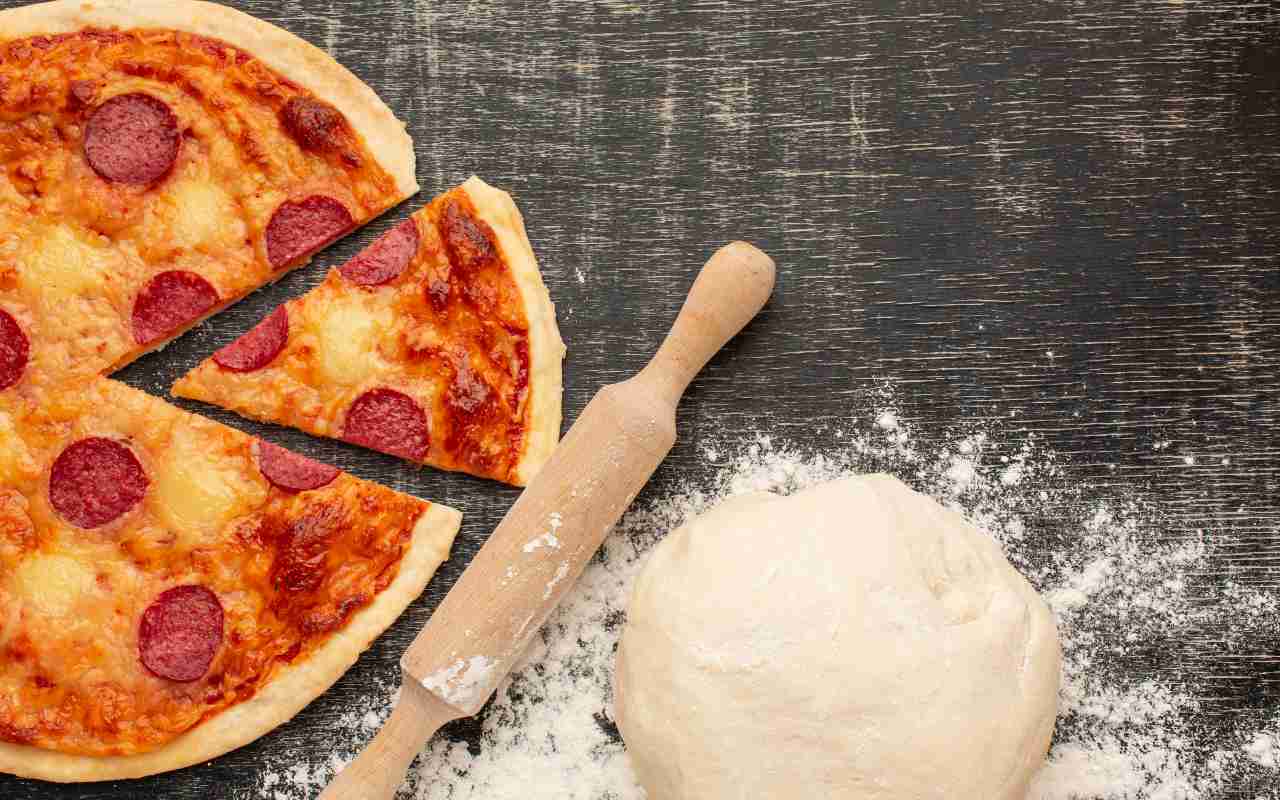 Una pizza alla diavola su un tavolo accanto a un mattarello e all'impasto per pizza